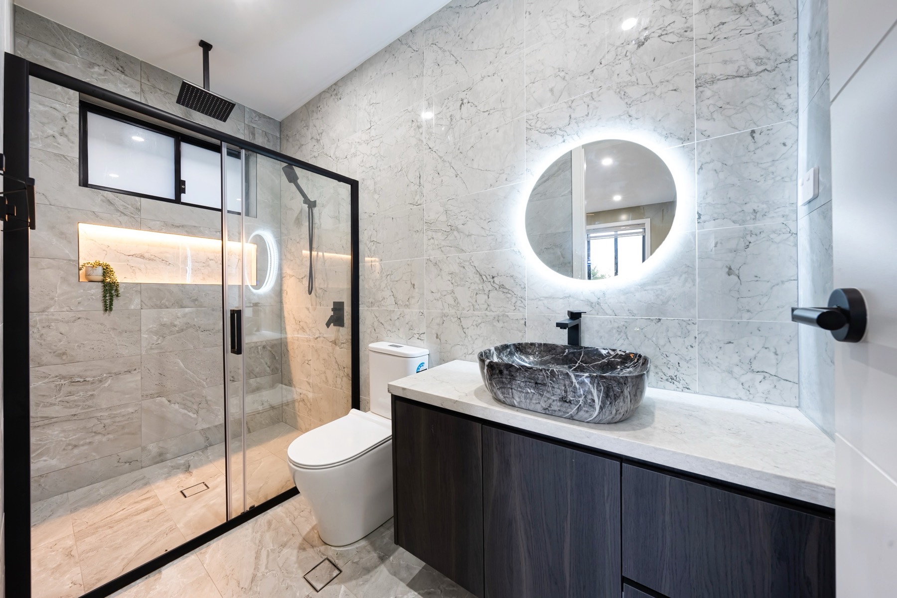 Sydney TCE bathroom with marble-look tiles, black fixtures and illuminated mirror